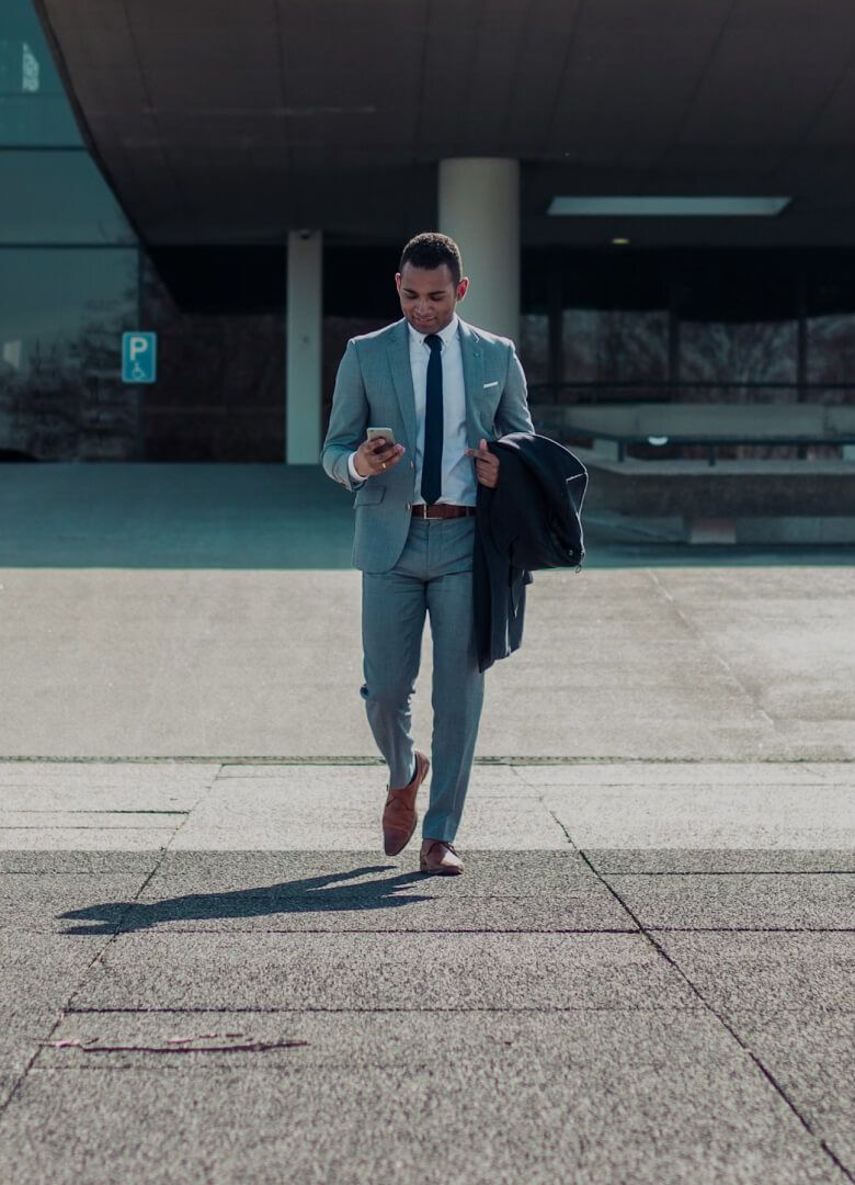Businessman in suit walking outside office, checking phone- Neutrinos