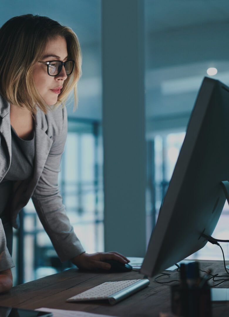 Woman in grey blazer working late on desktop computer in modern office - Neutrinos