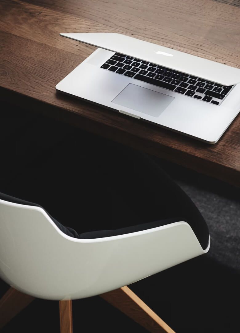 Modern workspace with a partially closed laptop on a wooden desk and a white chair with wooden legs-Neutrinos