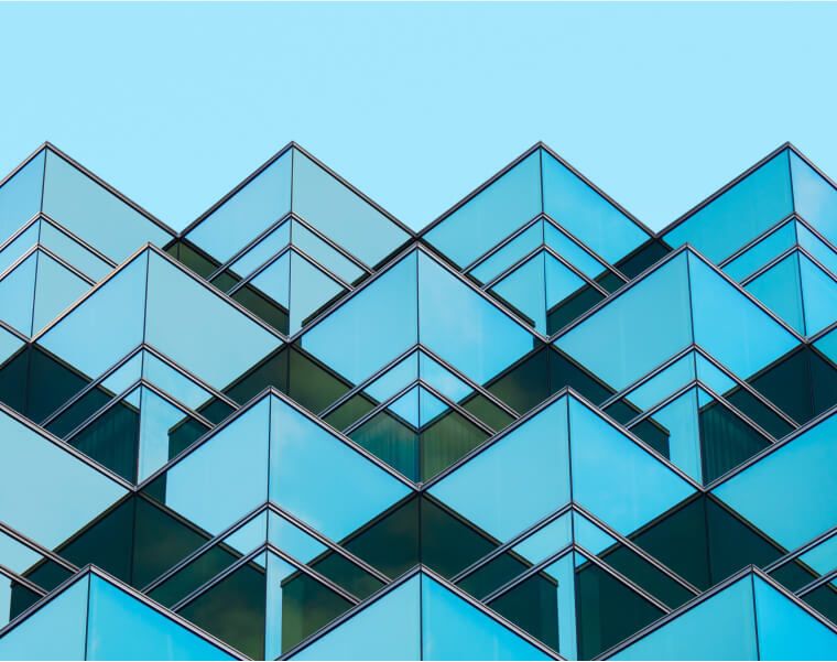 Modern glass building facade with geometric, angular balconies against a clear blue sky-Neutrinos