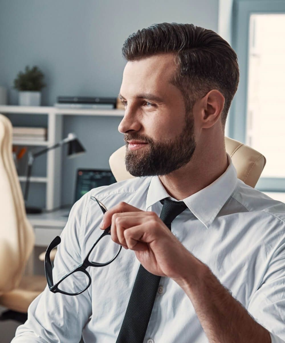 Professional man in shirt and tie holding eyeglasses, looking thoughtfully to the side - Neutrinos