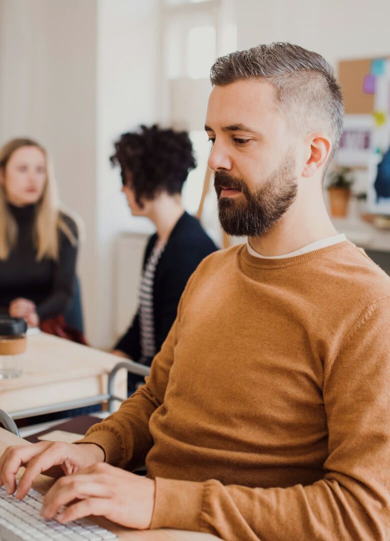 Man in brown sweater working on a computer in a modern office setting- Neutrinos